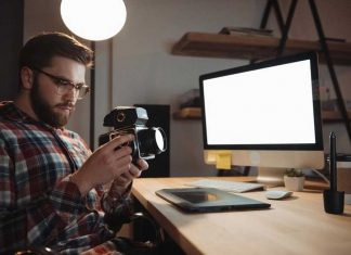 man sitting at desk in front of computer holding camera